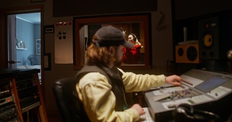 Working in a recording studio. The sound engineer uses an audio mixer. The singer sings into the...