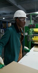 A man works in a paper mill. He talks to his colleague as he stacks the sliced cardboard