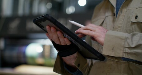 A man uses a tablet while working at a factory. Close-up of his hands, an unrecognizable person