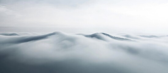Obraz premium Foggy mountain peaks under a cloudy sky, abstract aerial landscape with soft light and smooth textures
