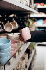 Man holding pink ceramic cup from a shelf in homeware store.