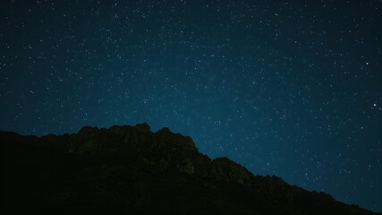 Starry Night over Mountains: A breathtaking long exposure photograph captures the mesmerizing dance of stars above a majestic mountain silhouette, creating a scene of serene beauty and cosmic wonder.
