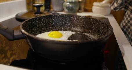 A man is frying eggs in a frying pan, he adds spices. Cooking breakfast at home. Close-up of his hand, an unrecognizable person