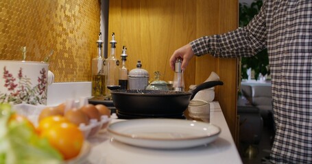 A man is frying eggs in a frying pan, he adds spices. Cooking breakfast at home. Close-up of his hand, an unrecognizable person