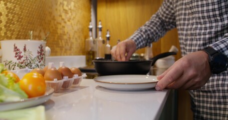 The man puts the cooked fried eggs from the pan into a plate. Close-up of his hands, an unrecognizable person