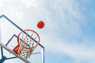 Basketball shoots through hoop into clear blue sky above outdoor court during sunny day