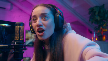 Happy Caucasian girl woman winner playing virtual game computer speaking microphone influencer female gamer winning match cyber sport gold champion receive cup addict streamer celebrate at home neon