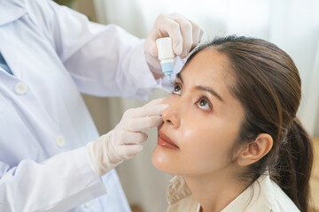 Health care concept, eye doctor eye drops to asian young woman patient, hand using medical eye drop...