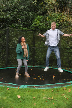 Mother and adult son jumping on trampoline in backyard
