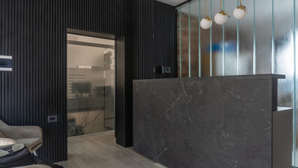 Modern office reception with dark paneling, a sleek grey stone reception desk, and a cozy waiting area with a soft grey armchair. The minimalist design creates a sophisticated and welcoming atmosphere