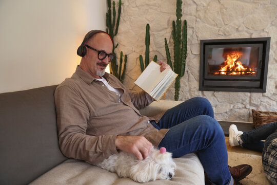Man sitting on sofa next to dog and reading