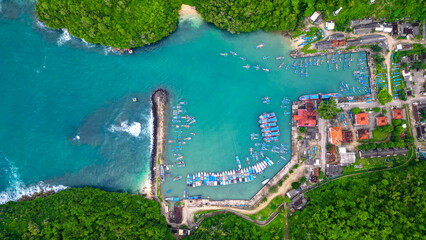 A breathtaking view of Sadeng Beach Pier, where dozens of fishing boats dock along the harbor, blending beautifully with green mountains and the vast blue ocean.