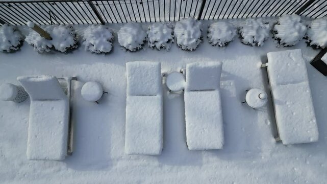 aerial view of snow covered lounge chairs next to closed shuttered swimming pool in winter (back yard patio loungers outdoor furniture) spa bizzard snowy snowfall frozen home countryside drone footage