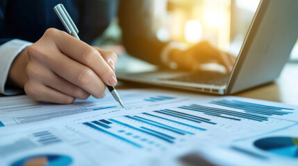 A financial analyst reviewing business charts and graphs on paper, with an open laptop in the background, symbolizing professional work. The image focuses on the hands doing detailed ink work