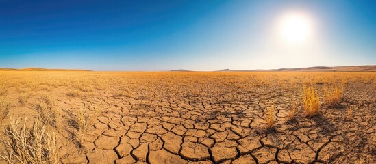 Barren dry landscape with cracked ground under clear blue sky and bright sun in arid environment showcasing drought conditions Copy Space
