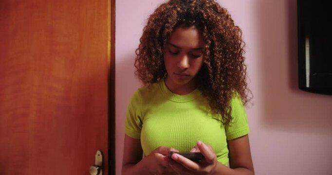 Teenager leans against wall engrossed in cellphone, emotional detachment and technology dependence shown, highlighting solitude and youth culture