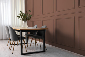 Table and chairs near mocha mousse shade wall indoors. Interior with trendy color of 2025 year