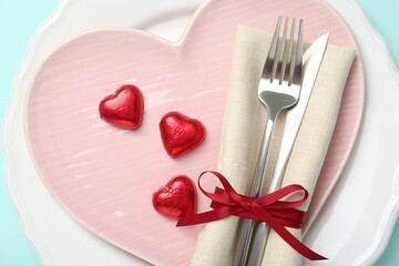 Romantic place setting with cutlery and plates on light blue background, top view. Valentine's day celebration