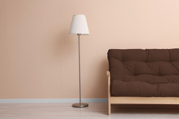Sofa in mocha mousse shade and floor lamp near beige wall indoors. Interior with trendy color of 2025 year
