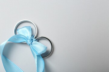 Silver wedding rings tied with ribbon on light grey background, top view. Space for text