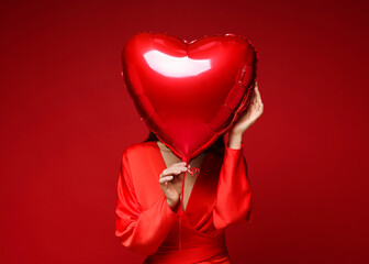 Happy Valentine's Day. Woman hiding behind heart shaped balloon on red background