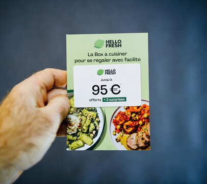 Paris, France - Jan 10, 2025: A hand holds a HelloFresh promotional card offering up to 95 euros in discounts and three surprises, showcasing appetizing meal images on a green background.