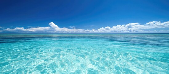 Crystal clear turquoise ocean water under a bright blue sky with white fluffy clouds and horizon line, Copy Space