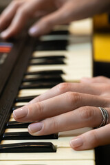 Obraz premium Close-up view of a musician's hand skillfully playing a vintage synthesizer, crafting electronic music in a cozy home studio, dressed in a stylish striped sweater. Vertical photo