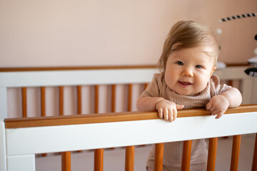 Cute Caucasian baby girl laughing standing in her crib. Portrait of laughing happy healthy 7 month old baby girl