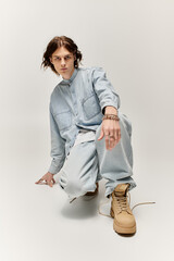 A fashionable young man kneels gracefully in casual attire, showcasing his unique style and flair.