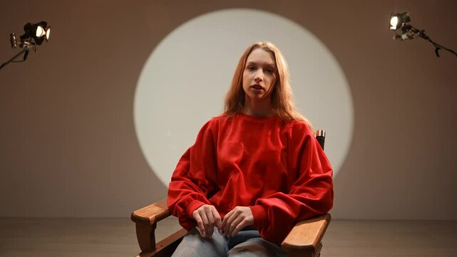 Studio for photo video production filming with lighting equipment and cyclorama, close shot of clapperboard with scene information, actress sits on chair and talks.