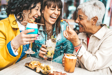 Happy senior women drinking cocktail glasses sitting at bar table - Group of best friends enjoying happy hour cheering drinks at pub restaurant - Life style concept with girls hanging out together