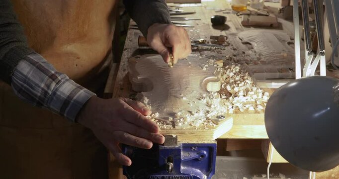Luthier working on the top plate of a violin using a gouge to smooth in his workshop