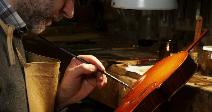 Luthier carefully applying varnish on a new handcrafted violin in his workshop in Cremona, Italy