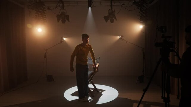 Studio for photo video production with lighting equipment and cyclorama, model actor sits on director chair in the middle and recording interview.