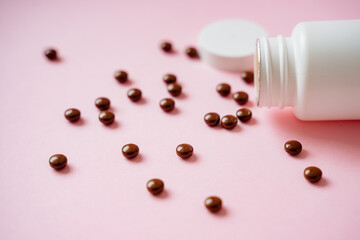 A bottle filled to the brim with a variety of colorful pills spills out onto a soft pink surface, creating an intriguing and visually appealing display of vibrant colors and unique shapes