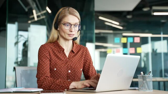 Woman in wireless headset customer service representative operator talking on video call on laptop sitting in office. Agent of the call center advises client, answering questions. Online consultation
