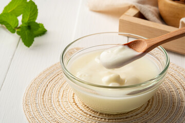 Close up low calorie yogurt in wooden spoon with yogurt in glass bowl