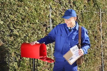 Postman putting parcel into mail box outdoors