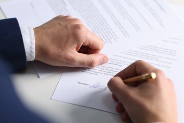 Man putting signature on document at table, closeup