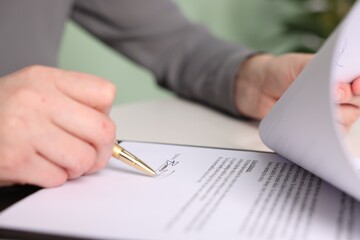 Woman putting signature on document at table, closeup