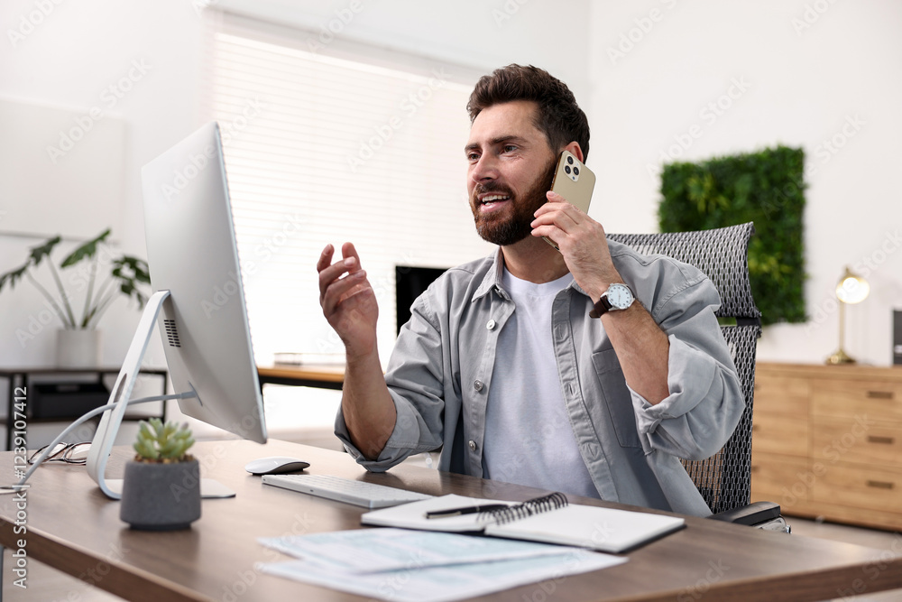 Poster man talking on smartphone while working at table in office