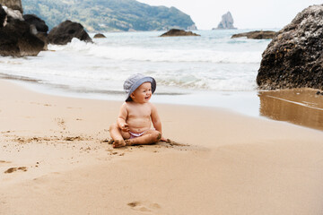 Smiling baby crawling and playing on seaside. Happy little child playing on beach near ocean.