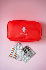 A vibrant red first aid kit is completely filled with various kinds of pills and capsules, prominently placed against a soft pink background, creating a striking visual effect
