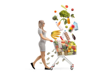 Young blond woman pushing a shopping cart with falling food products and walking