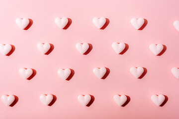 White heart-shaped candies with sharp shadows arranged in a grid on a pink background, symbolizing sweetness and love. Texture, background