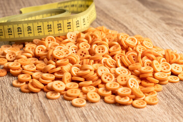 una huincha de medir amarilla con números negros sobre una pila de pequeños botones naranjos, fondo madera