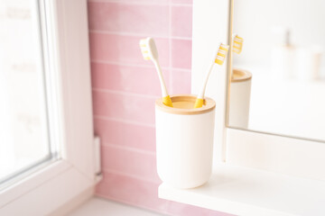 Two yellow toothbrushes in holder in bathroom on pink background.