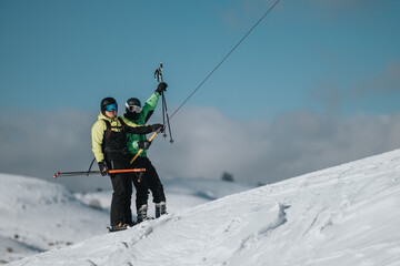 Two individuals on skis ascend a snowy slope side on a ski lift, surrounded by crisp, clear winter...