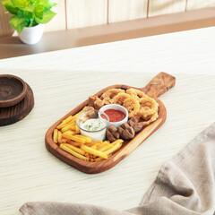 A wooden serving board features fried snacks like onion rings, potatoes, and sauces in a bright, welcoming indoor atmosphere